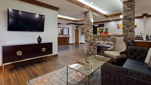 A spacious living area with a flat-screen TV, a stone fireplace, and comfortable seating. - Best Western Inn & Suites (Byron)