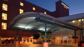 Hotel con patio, entrada cubierta, fachada de ladrillo y zona de estacionamiento bien iluminada.