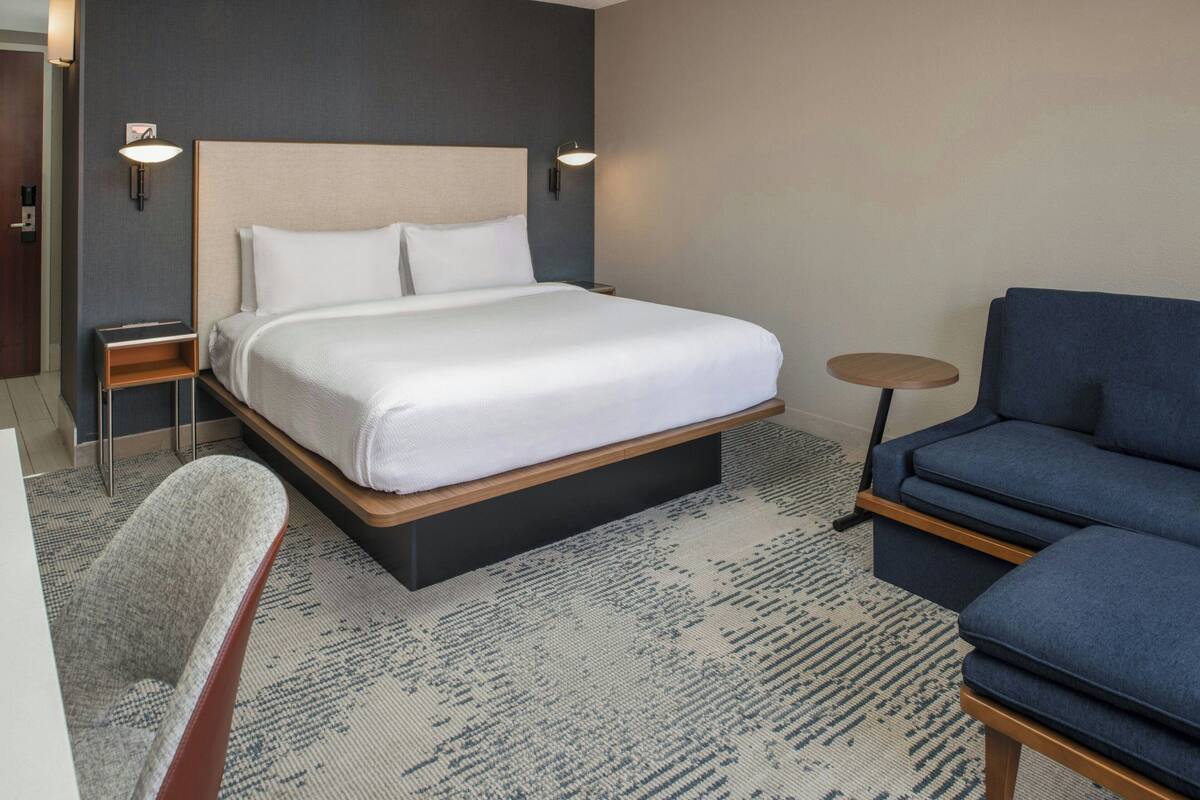 A hotel room with a large bed, a small round table, a blue sofa, and a chair.