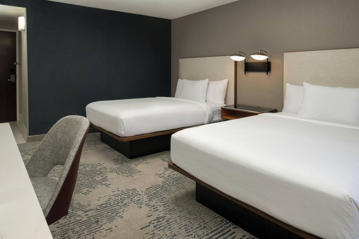 A hotel room with two beds, a desk, and a chair.