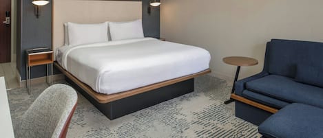 Una habitación de hotel con una cama grande, un sofá azul, una mesita redonda y una silla.