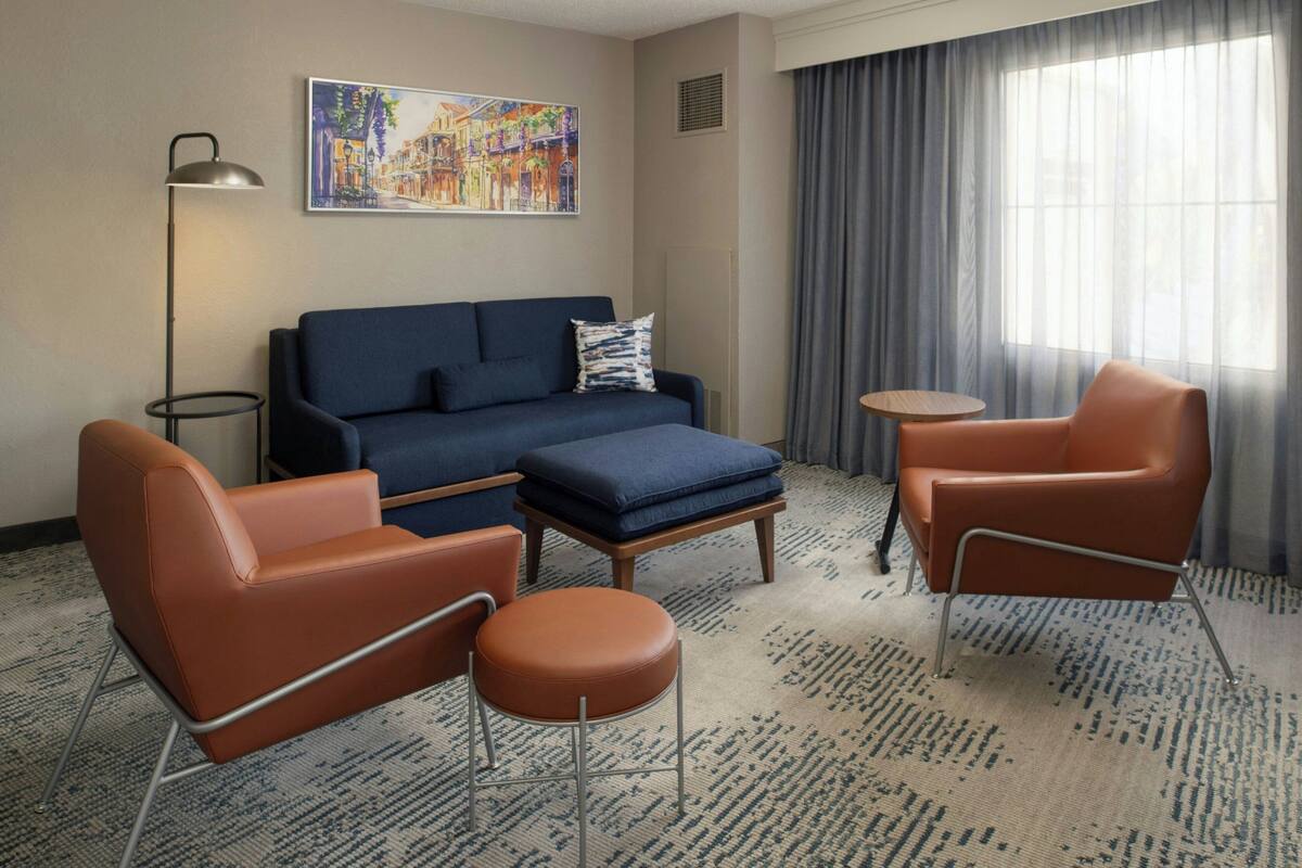 A hotel room with a blue sofa, two brown armchairs, a small round table, and a floor lamp.