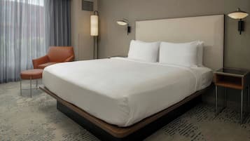 Una habitación de hotel con una cama grande, una silla, una mesita de noche y una lámpara.