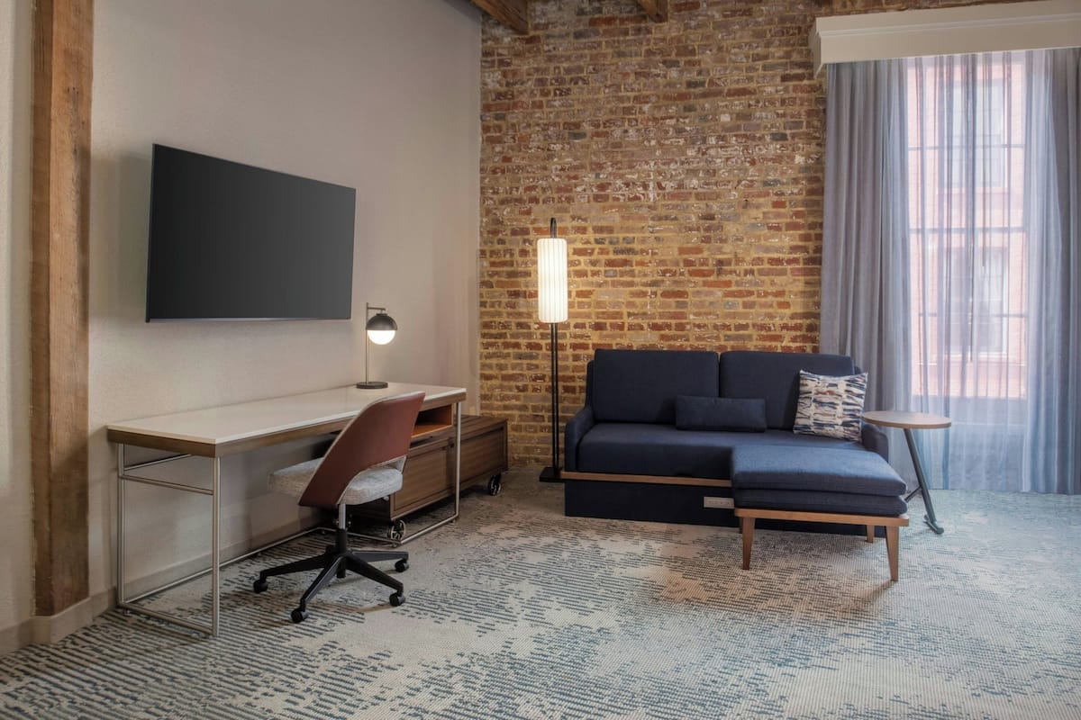 A room with a desk, chair, sofa, and a TV mounted on the wall.