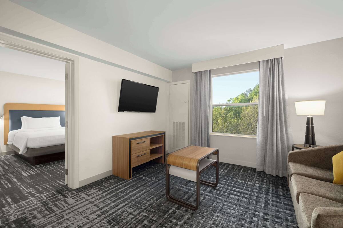 A hotel room with a bed, a desk, a TV, a window with curtains, and a sofa.