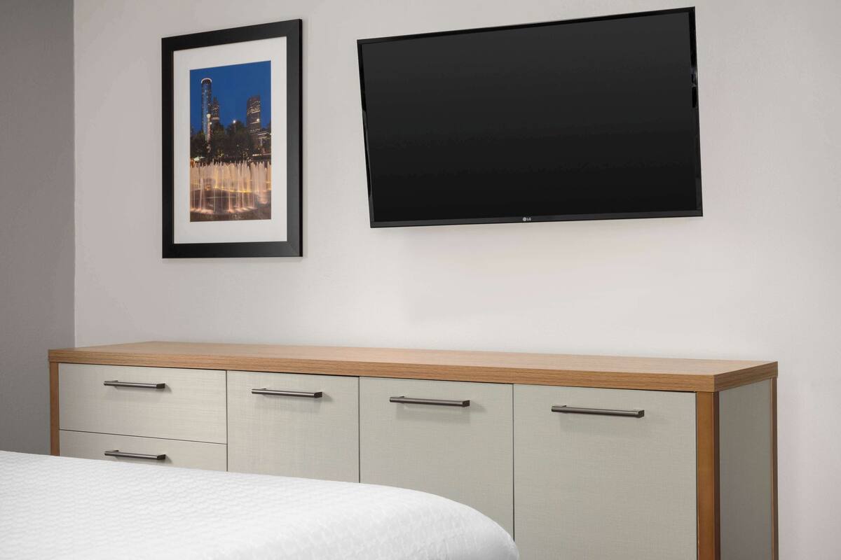 A bedroom with a bed, a wooden bedside table, a flat-screen TV, and a framed picture on the wall.