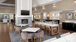 Un amplio vestíbulo de hotel con chimenea central, un área de comedor y una cocina.