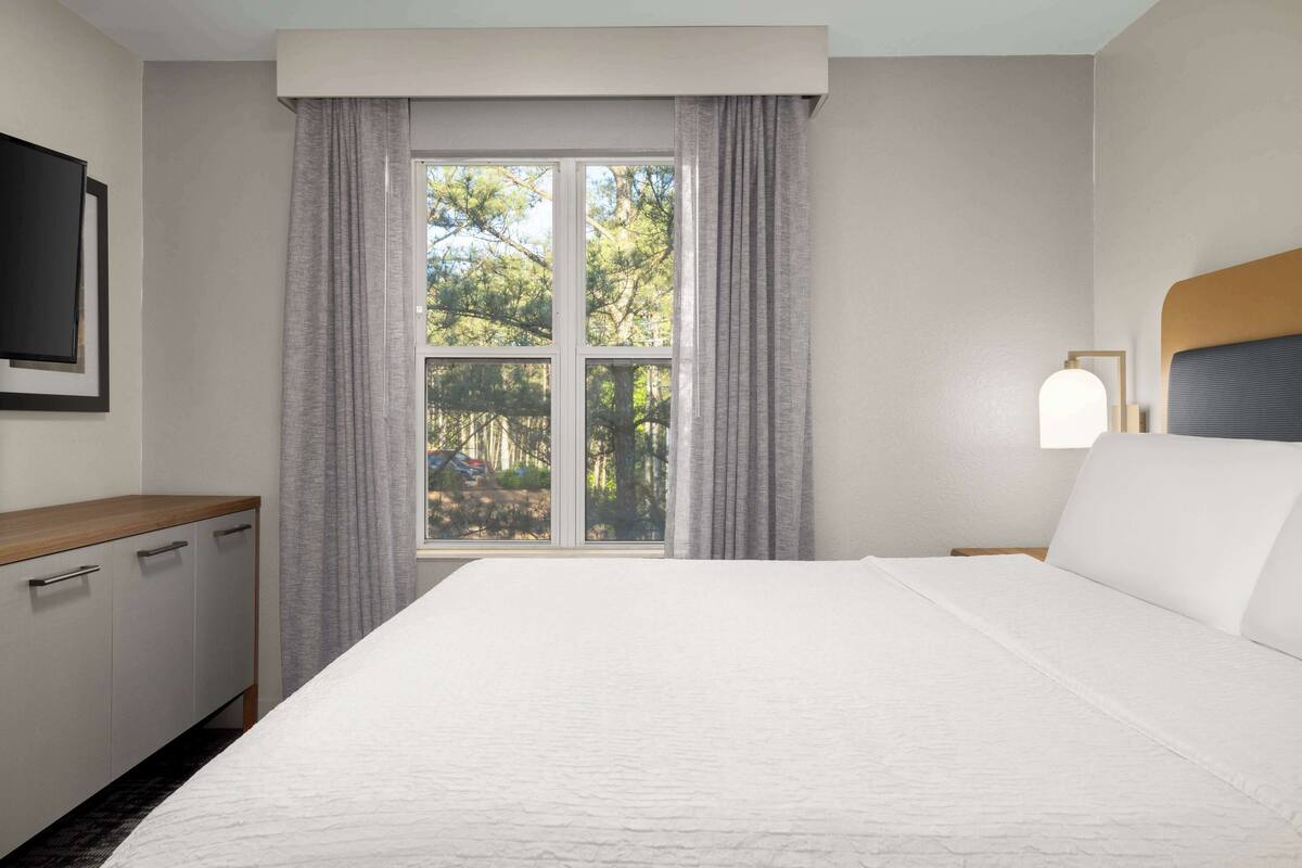 A hotel room with a large bed, a wooden desk, a television, and a window with curtains.