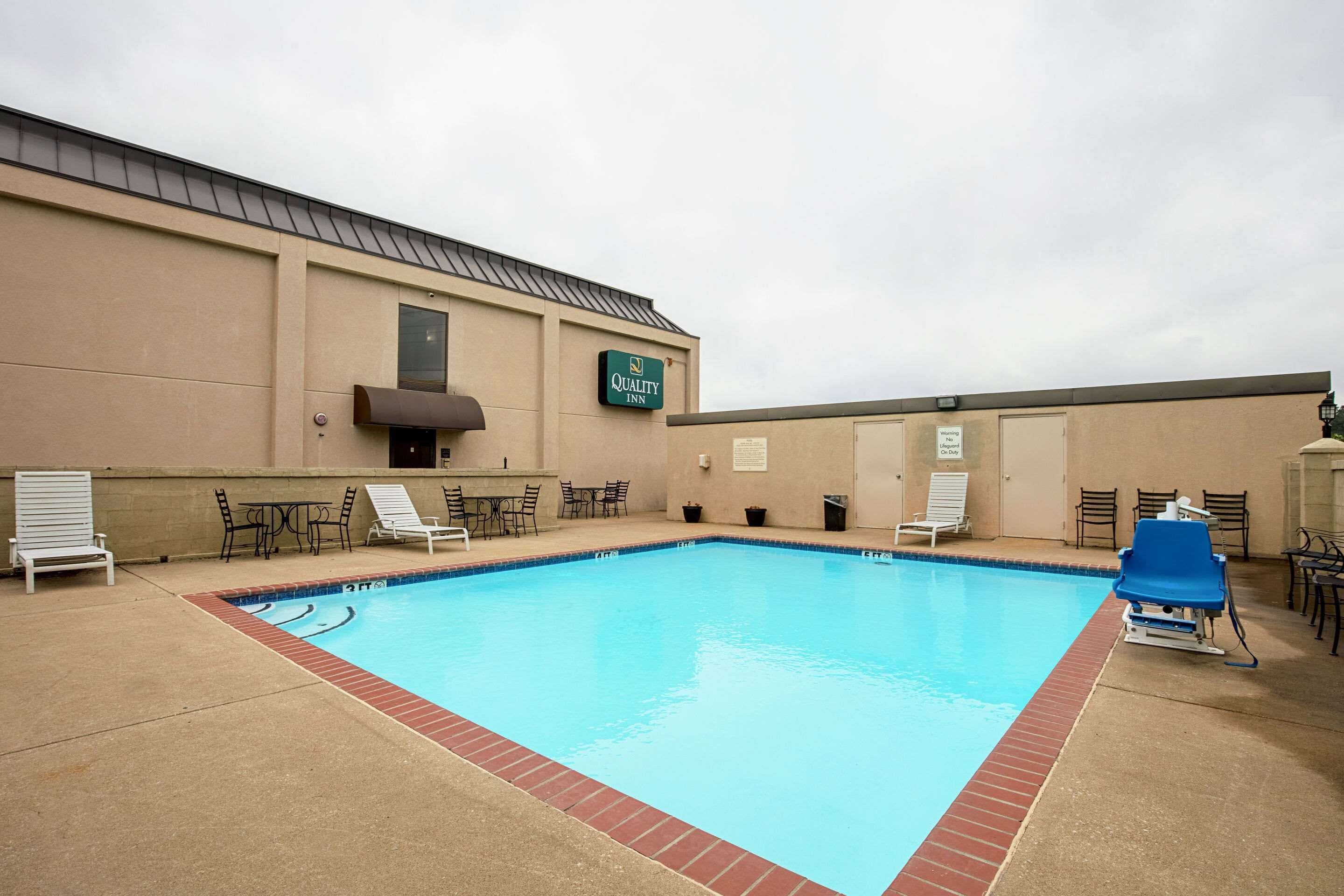 A swimming pool with lounge chairs and tables, a Quality Inn sign, and a covered seating area.