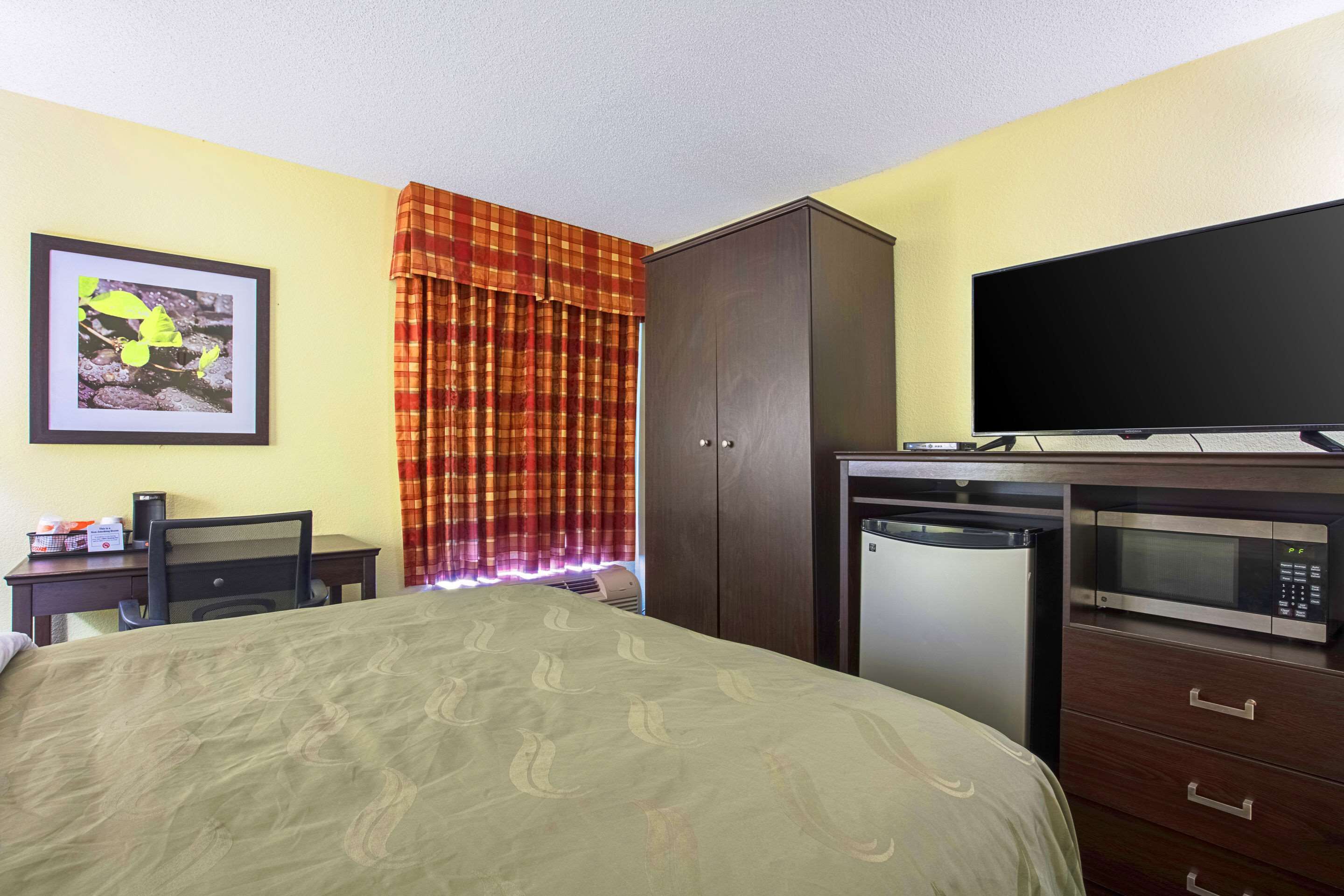 A hotel room with a bed, a desk with a computer, a microwave, and a television.