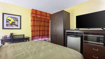 A hotel room with a bed, a desk with a computer, a microwave, and a television.