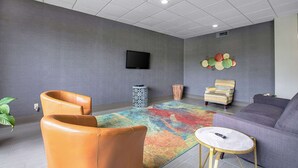 Een moderne woonkamer met een grijs gestructureerde muur, een flatscreen televisie boven een kamerkleed met patroon, een bank, twee leren fauteuils, een klein rond tafeltje en een decoratief wandobject.