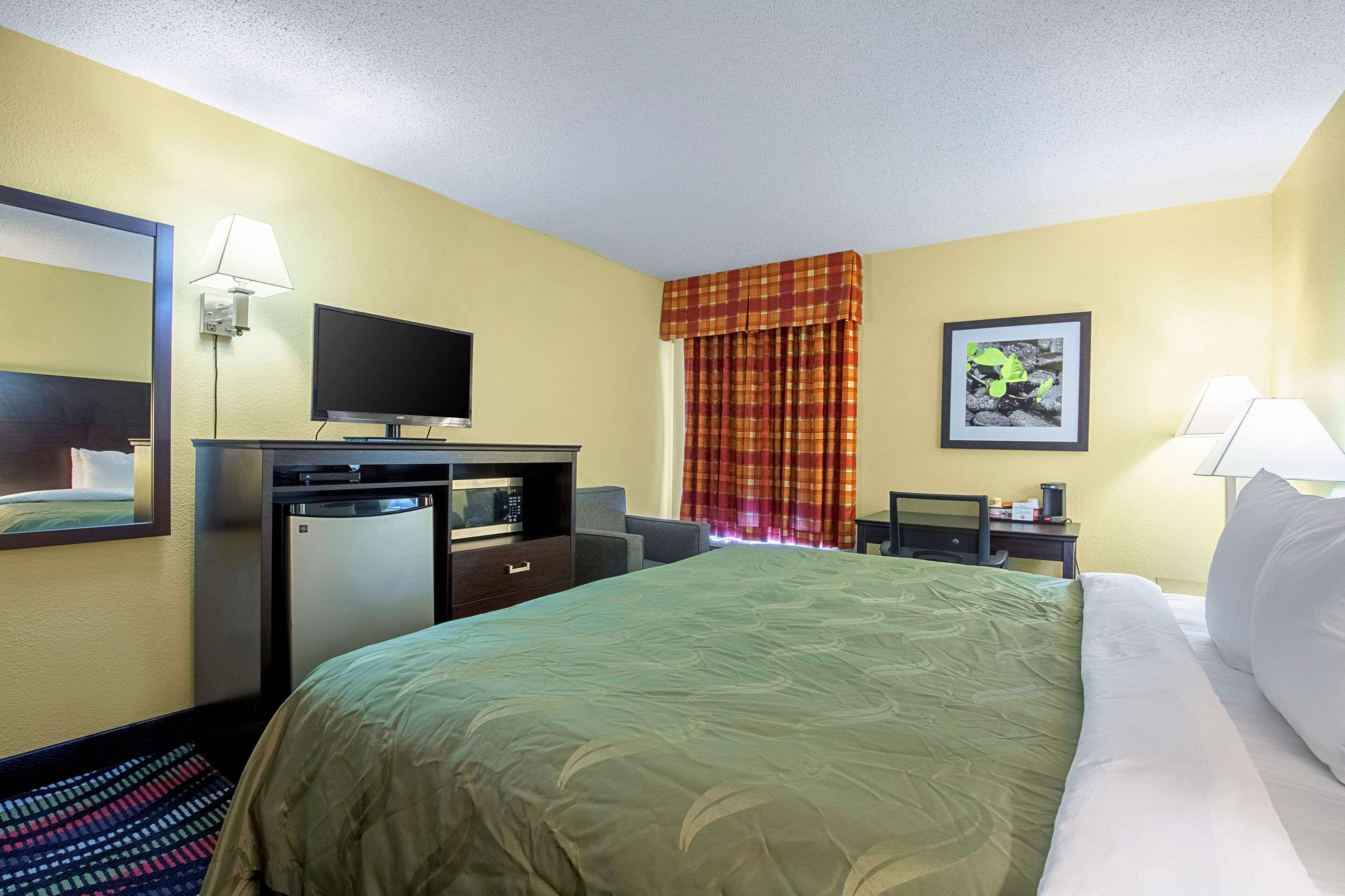 A hotel room with a bed, a TV, a desk, and a chair.