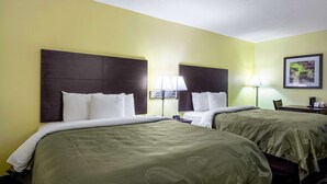 Een hotelkamer met twee bedden, elk voorzien van een donker hoofdeinde en witte beddengoed. Er staan twee nachtlampjes en een ingelijste foto aan de muur.