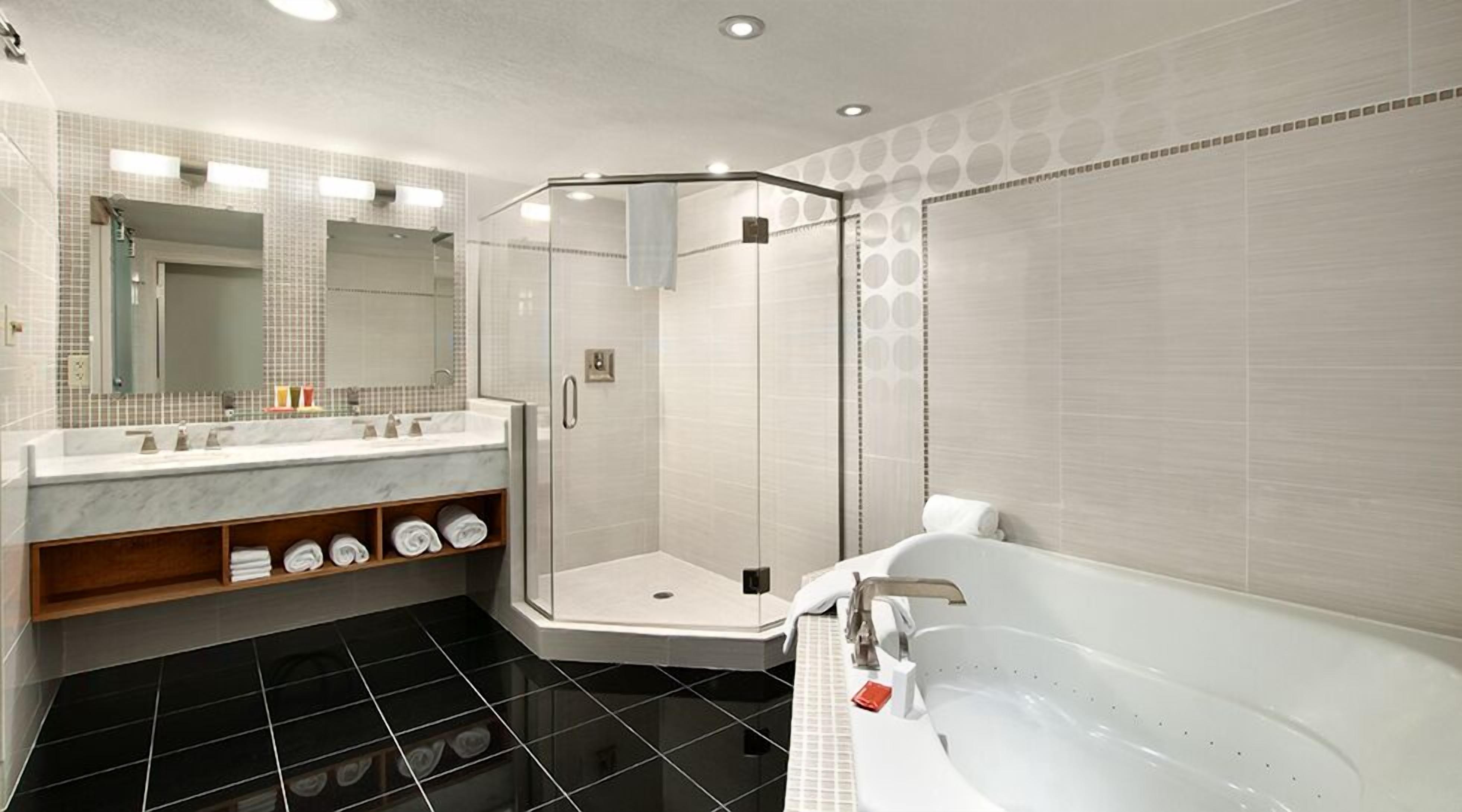A modern bathroom with a glass-enclosed shower, a large bathtub, and a marble vanity with a mirror.