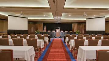 A conference room with rows of tables and chairs, a stage with a podium, and an American flag.