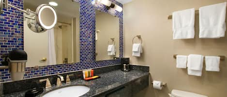 A bathroom with a blue-tiled wall, a sink, a mirror, a toilet, and multiple white towels hanging on the wall.