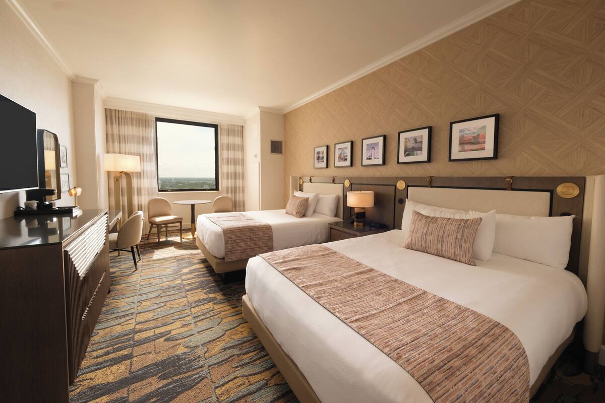 Habitación de hotel con dos camas, un escritorio, una silla y un ventanal grande.