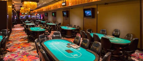 A casino with multiple blackjack tables, chairs, and slot machines.