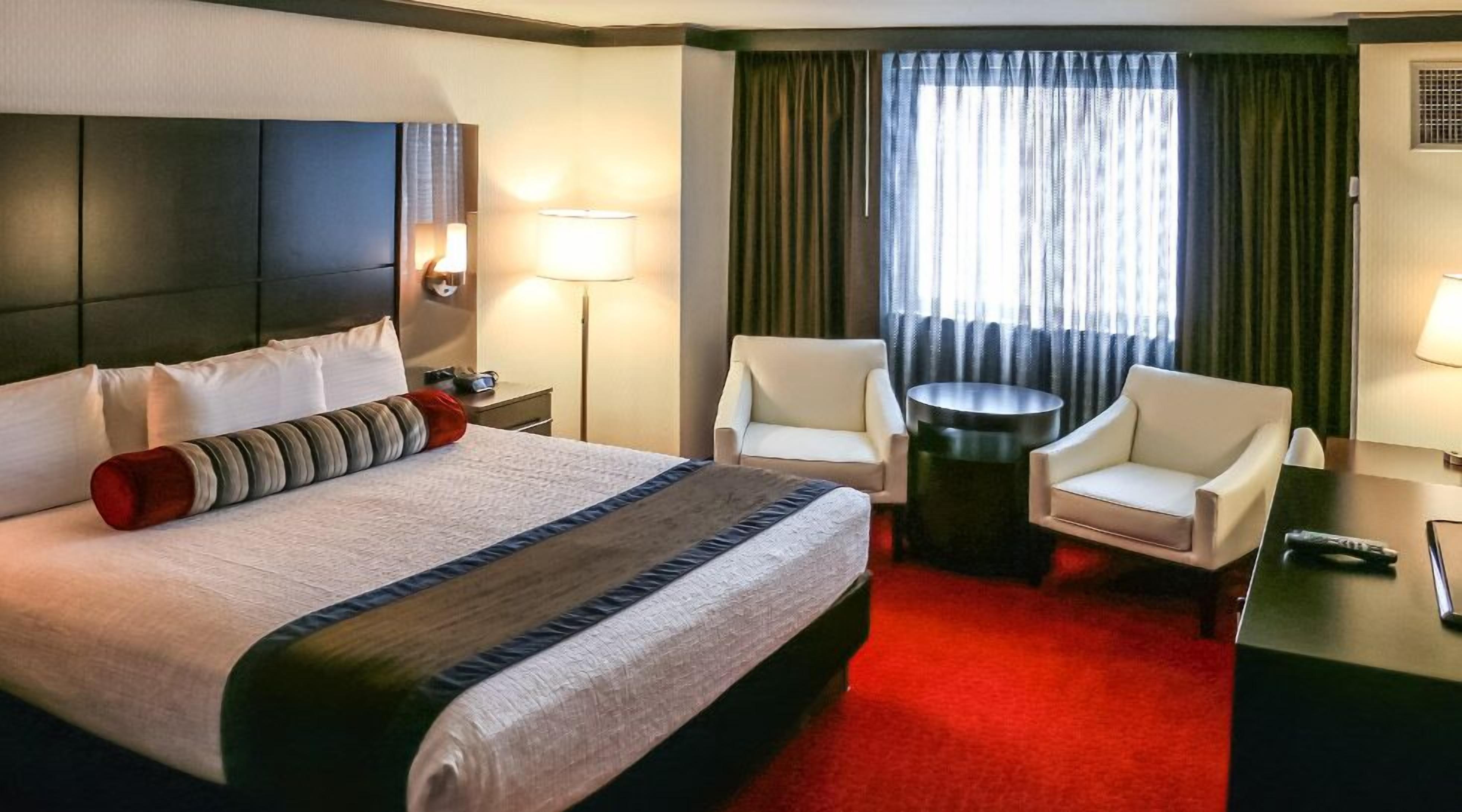 Habitación de hotel con una cama grande, dos sillones, una mesita redonda y un escritorio con lámpara.