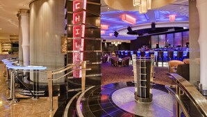 Un lobby moderno de hotel con una zona de bar, una escalera y un letrero de neón decorativo.