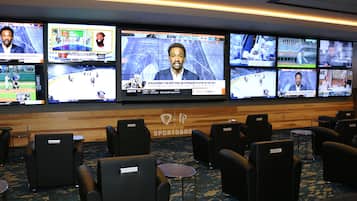 A sports lounge with multiple screens displaying various sports events, comfortable seating, and a wooden wall with the text "SPORTSBOO".