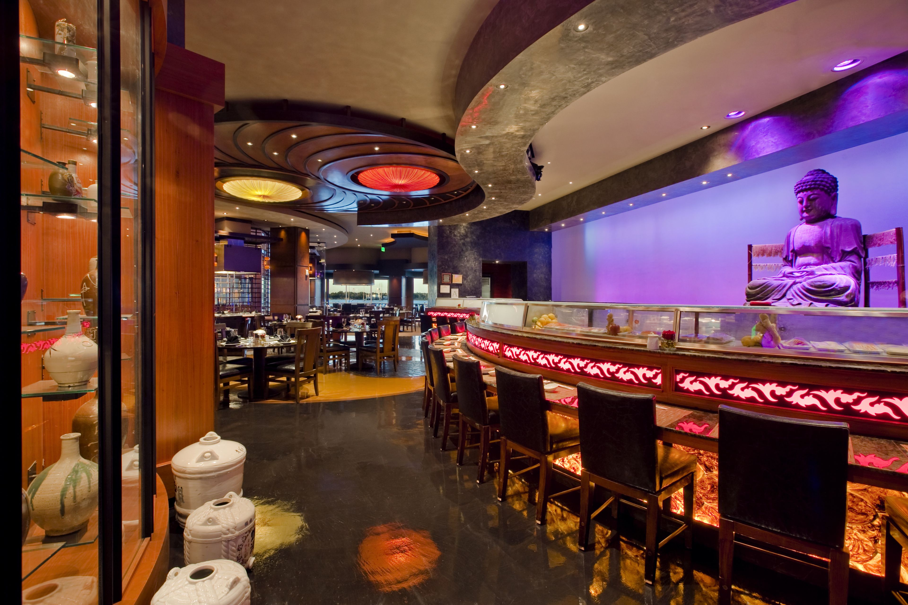 A restaurant with a Buddha statue, wooden decor, and a modern ceiling design.