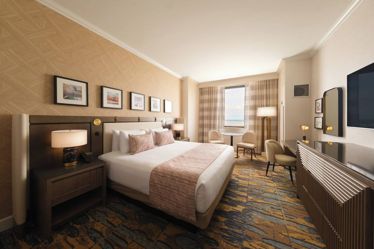 Habitación de hotel con una cama grande, un escritorio, una silla y vistas al exterior.