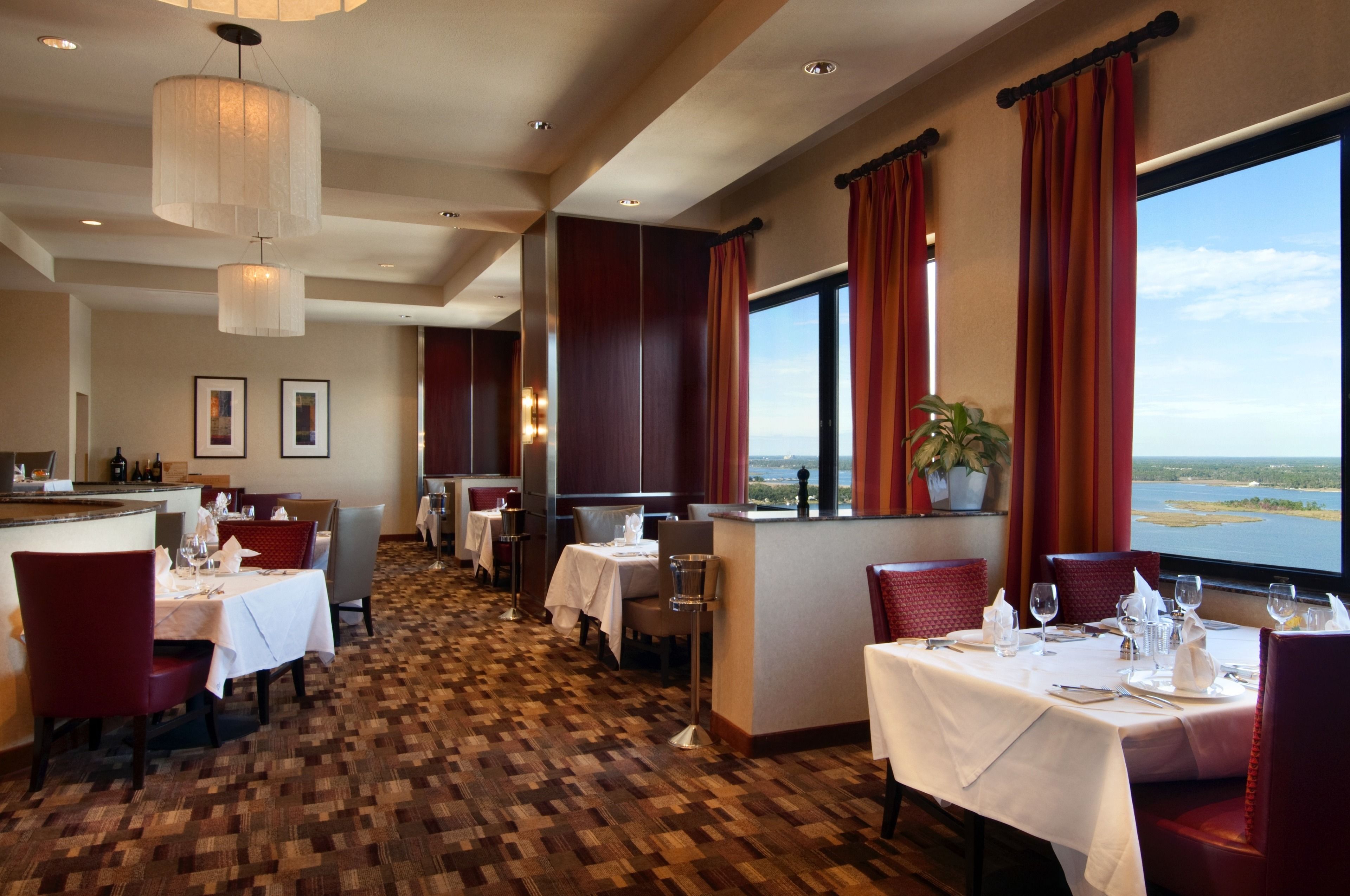 A restaurant with tables set for dining, a bar area, and a view of the water.