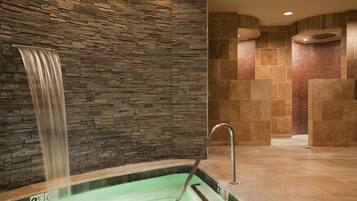 A spa area with a stone wall, a waterfall feature, and a tiled floor.