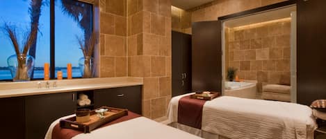 Un cuarto de spa con dos camas, un espejo grande y vistas a palmeras.