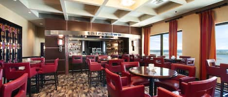A restaurant with red chairs and tables, a bar area, and large windows offering a view.