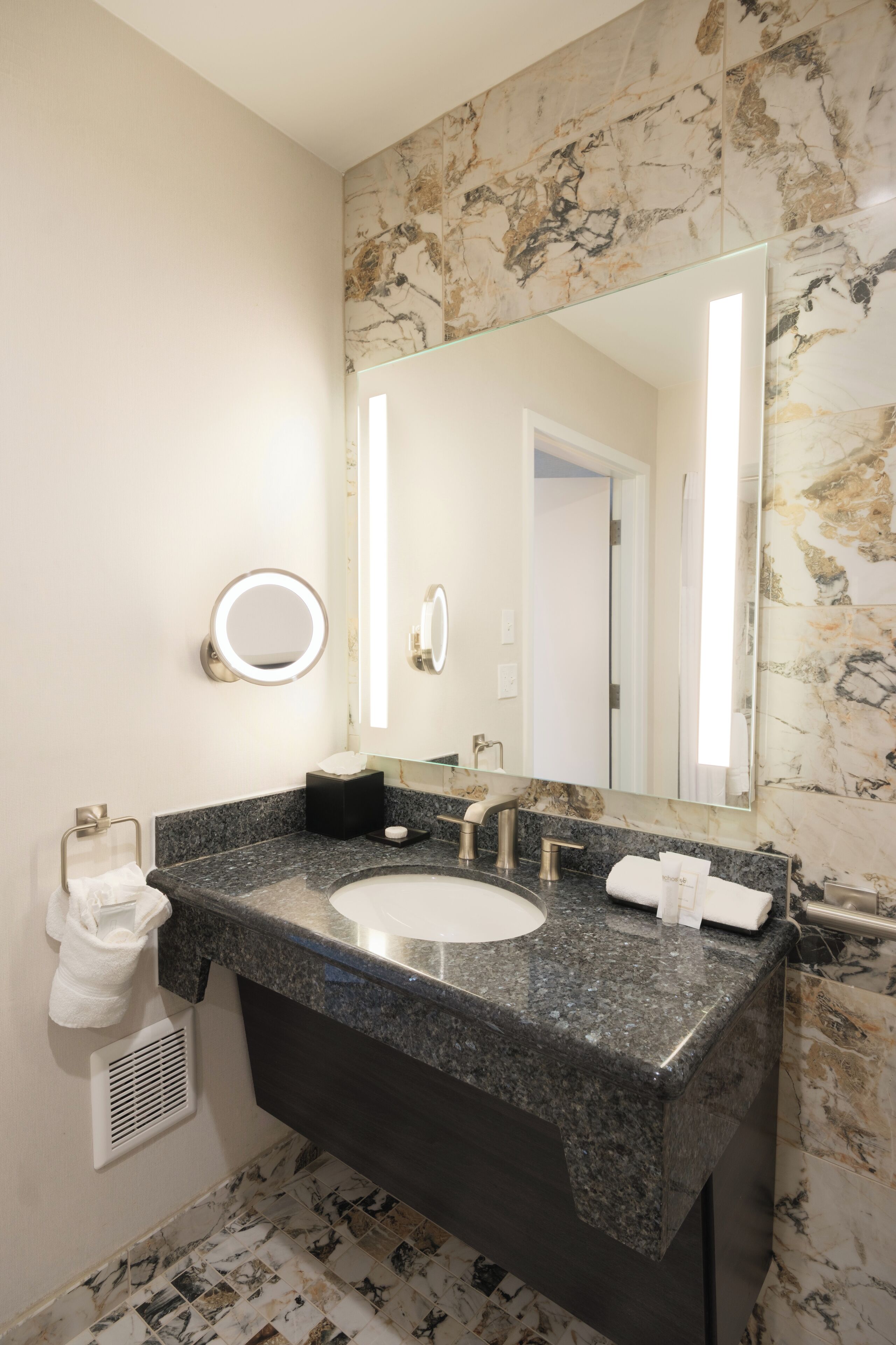Une salle de bain avec un lavabo en marbre, un grand miroir et un porte-serviettes.