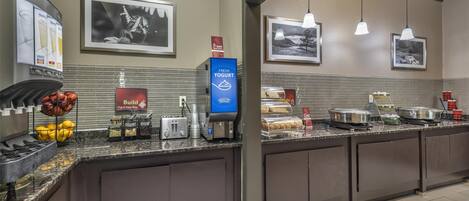 A hotel breakfast area with a self-serve station, including a coffee machine, toaster, and fruit bowl.
