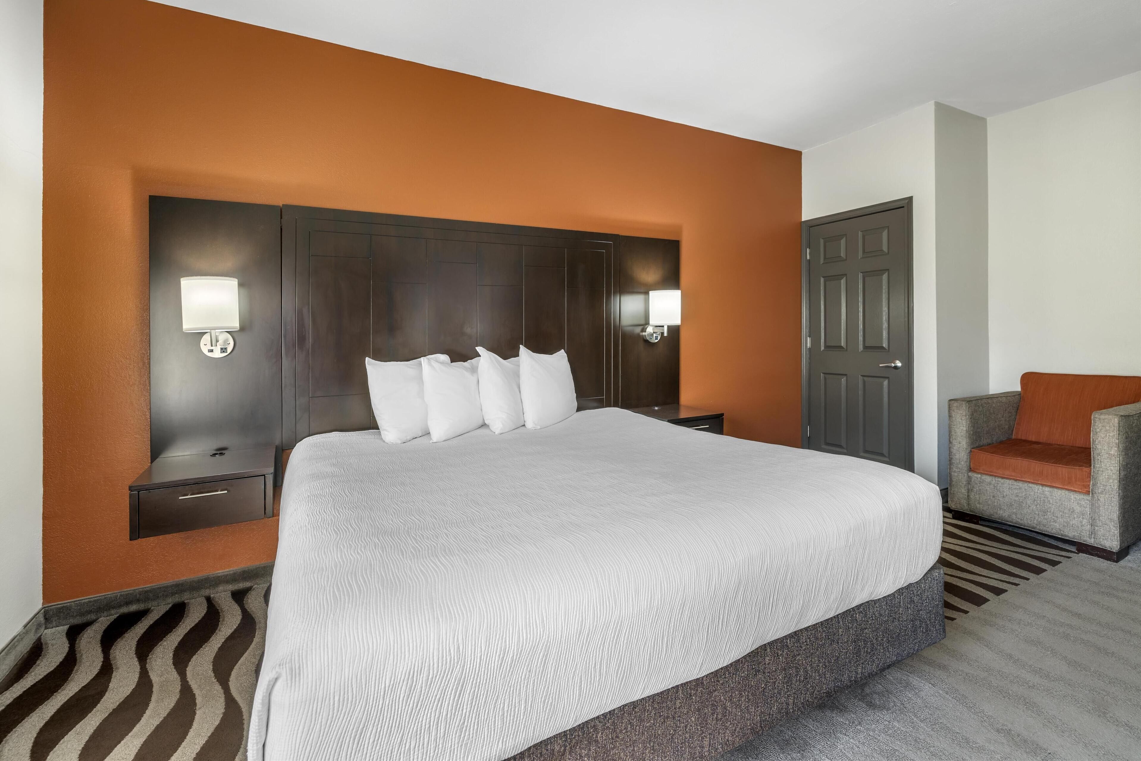A hotel room with a large bed, two bedside tables, a chair, and a door.