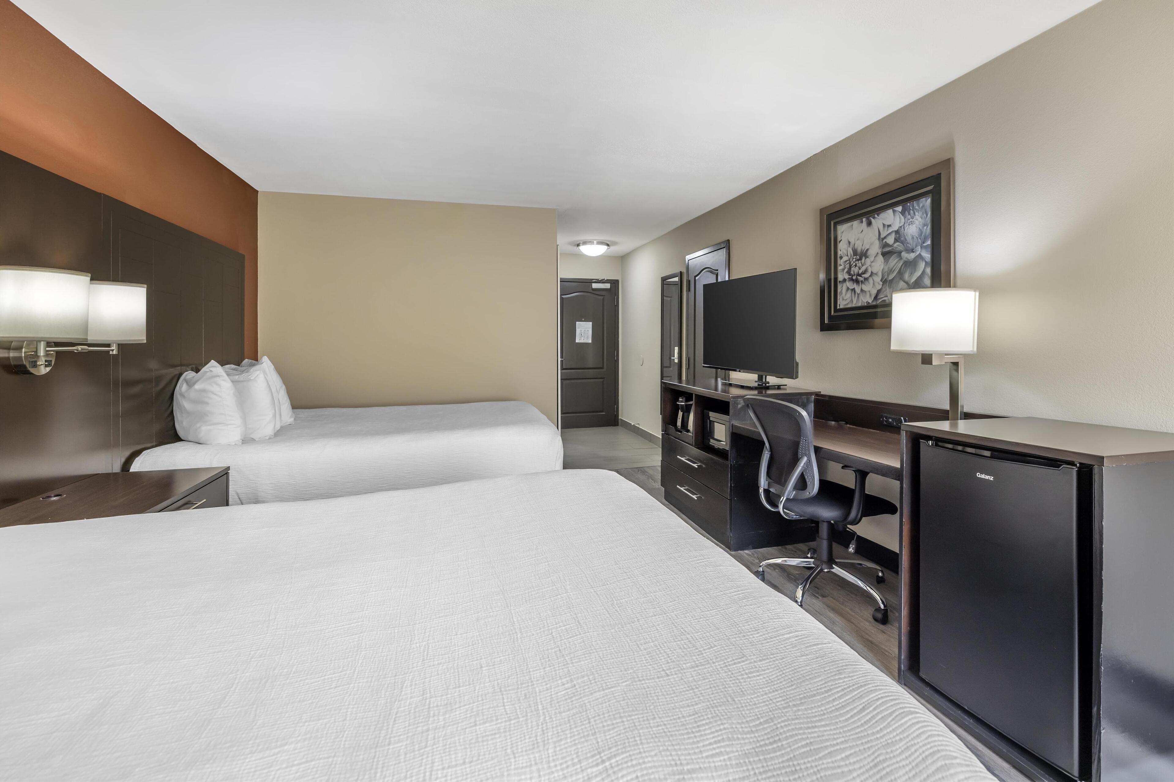 Habitación de hotel con dos camas, un escritorio con computadora, un refrigerador y un televisor.