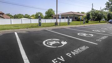 Un parking avec des places réservées aux véhicules électriques, un bâtiment en arrière-plan et une clôture blanche.