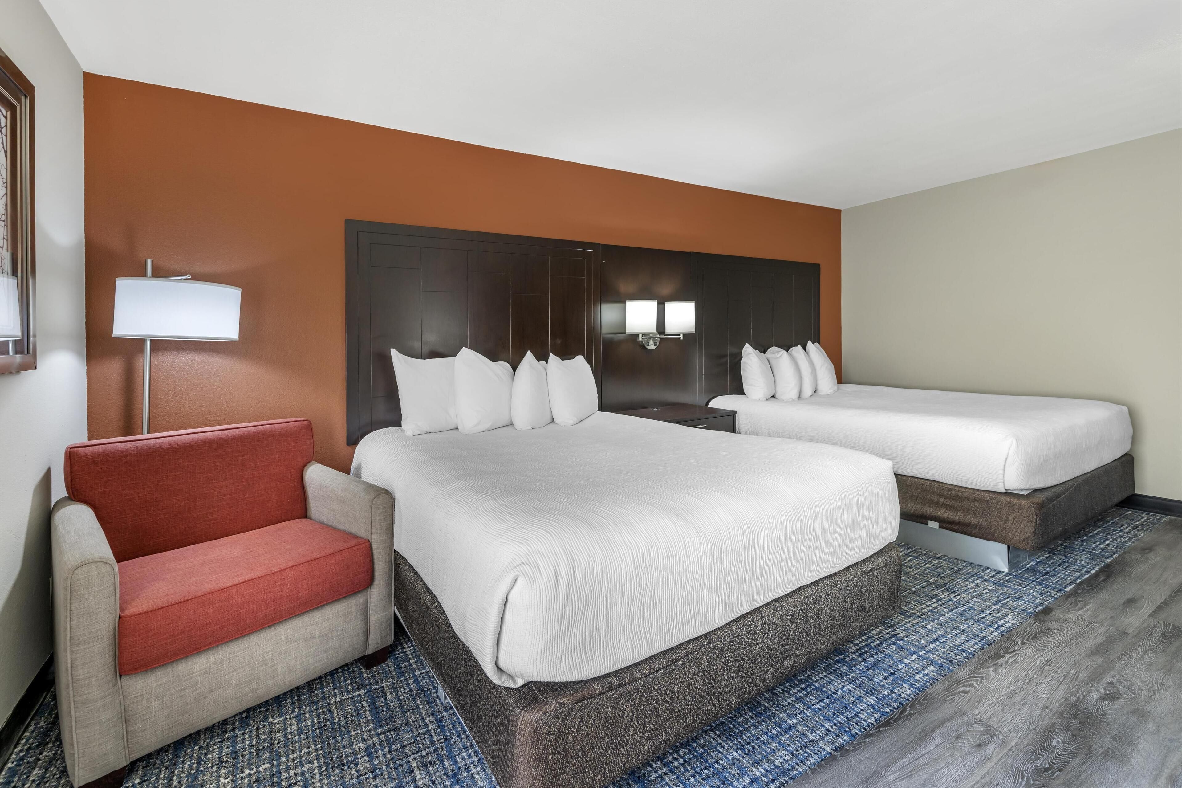 A hotel room with two beds, a sofa, and a lamp.