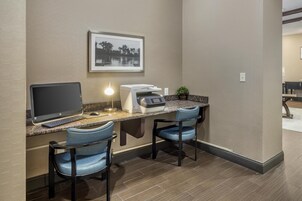 Habitación de hotel con escritorio, dos sillas, una computadora, una impresora y un cuadro en la pared.