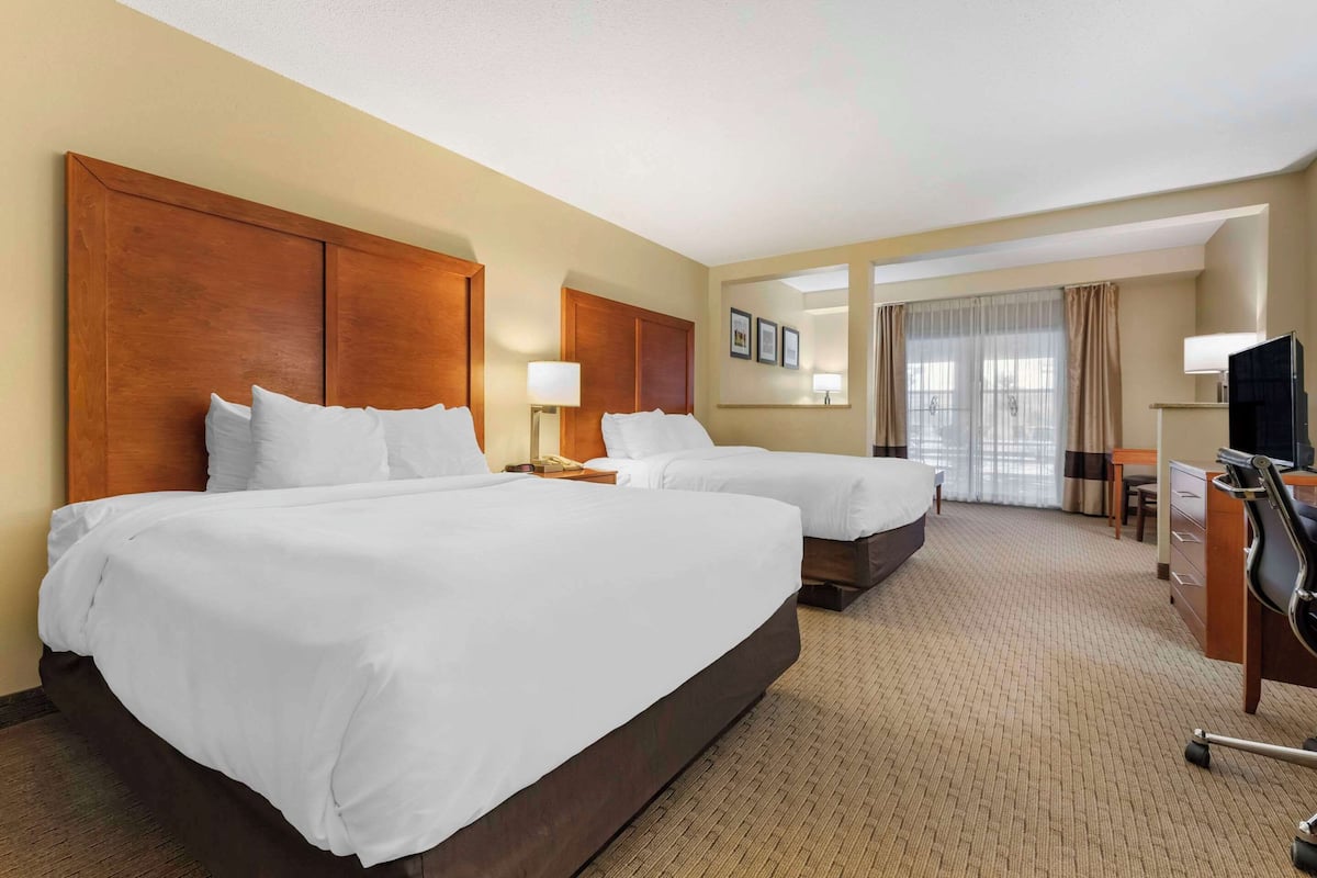 A hotel room with two beds, a desk, a chair, a TV, and a window with curtains.