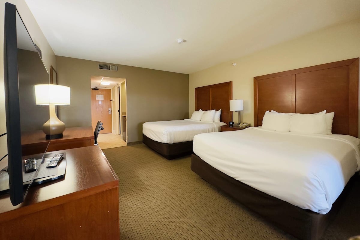 A hotel room with two beds, a desk with a lamp, and a television.