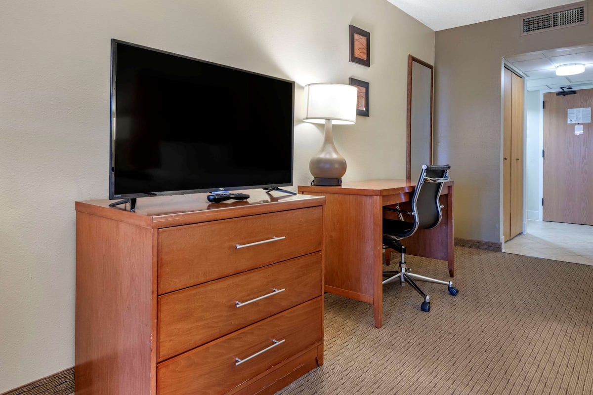 A hotel room with a wooden desk, a flat-screen TV, a lamp, and a chair.