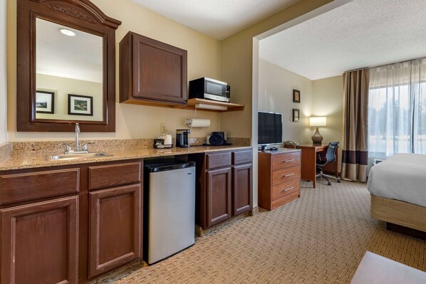 Habitación de hotel con kitchenette, que incluye microondas, cafetera y refrigerador. Cuenta con una cama, un escritorio con silla y una ventana con cortinas.