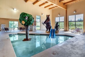 An indoor swimming pool with a bear statue, a tree sculpture, and a bear statue holding a fish.