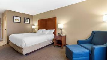 A hotel room with a bed, bedside table, lamp, and a blue armchair.