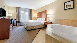 Habitación de hotel con cama, escritorio con computadora, televisor, baño con bañera y ventana con cortinas.