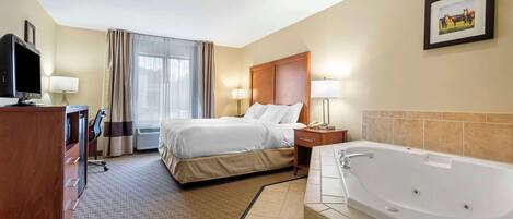 Habitación de hotel con cama, escritorio con computadora, televisor, baño con bañera y ventana con cortinas.