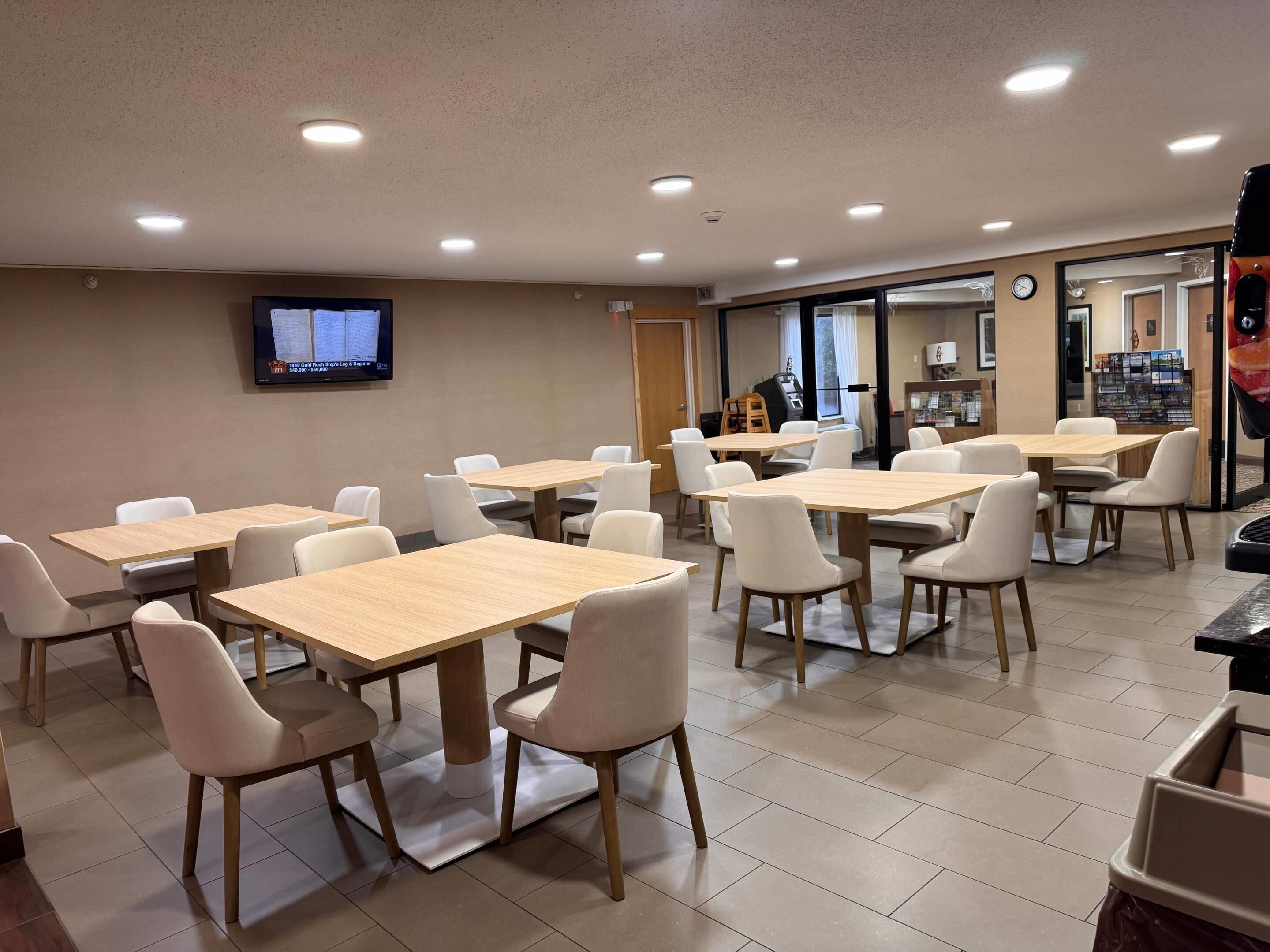 A conference room with multiple tables and chairs, a television on the wall, and a door leading to another area.
