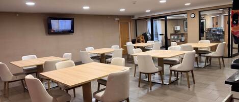A conference room with multiple tables and chairs, a television on the wall, and a door leading to another area.