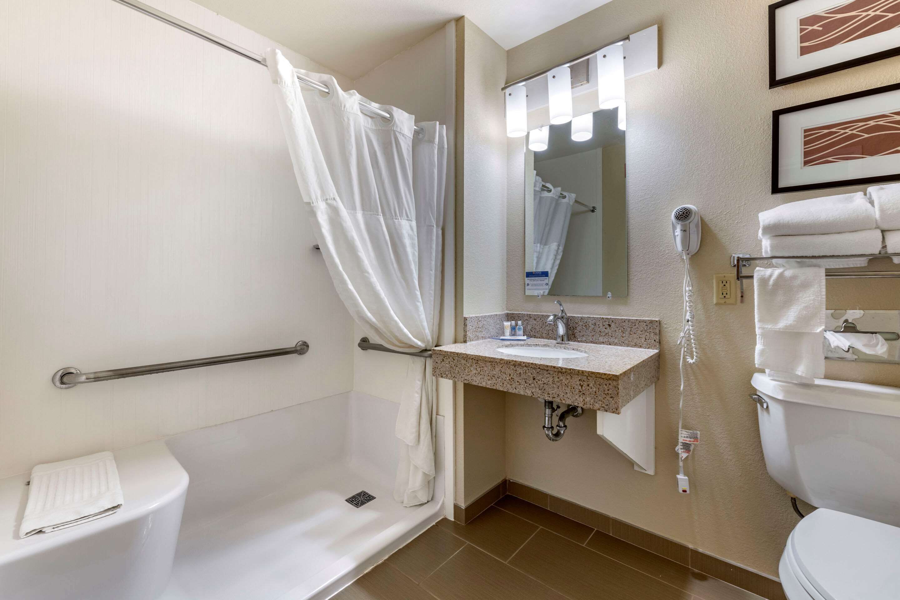 A bathroom with a shower, toilet, sink, and a hairdryer on the wall.